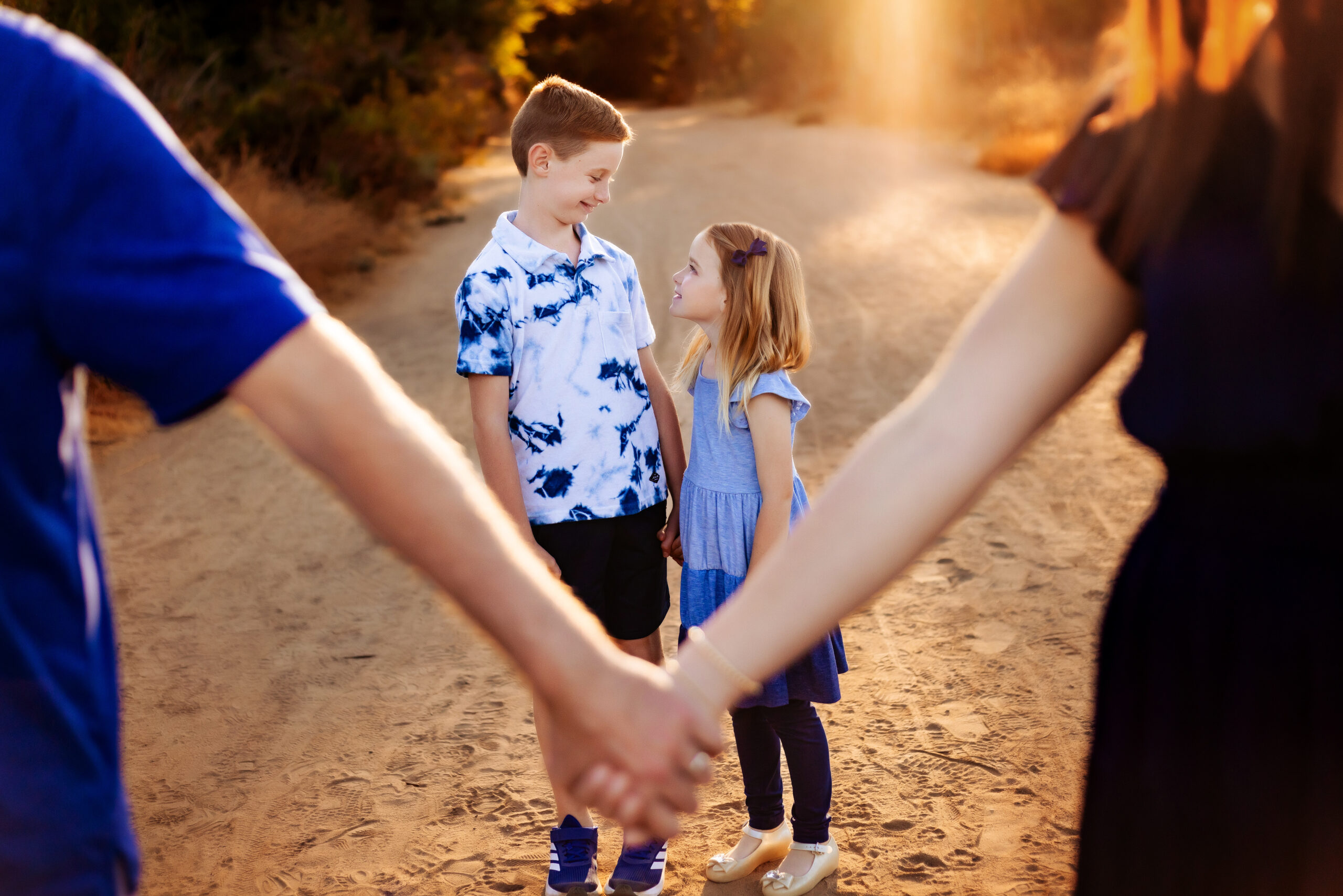 San Diego family session, a mom and dad hold hands while their children smile at each other